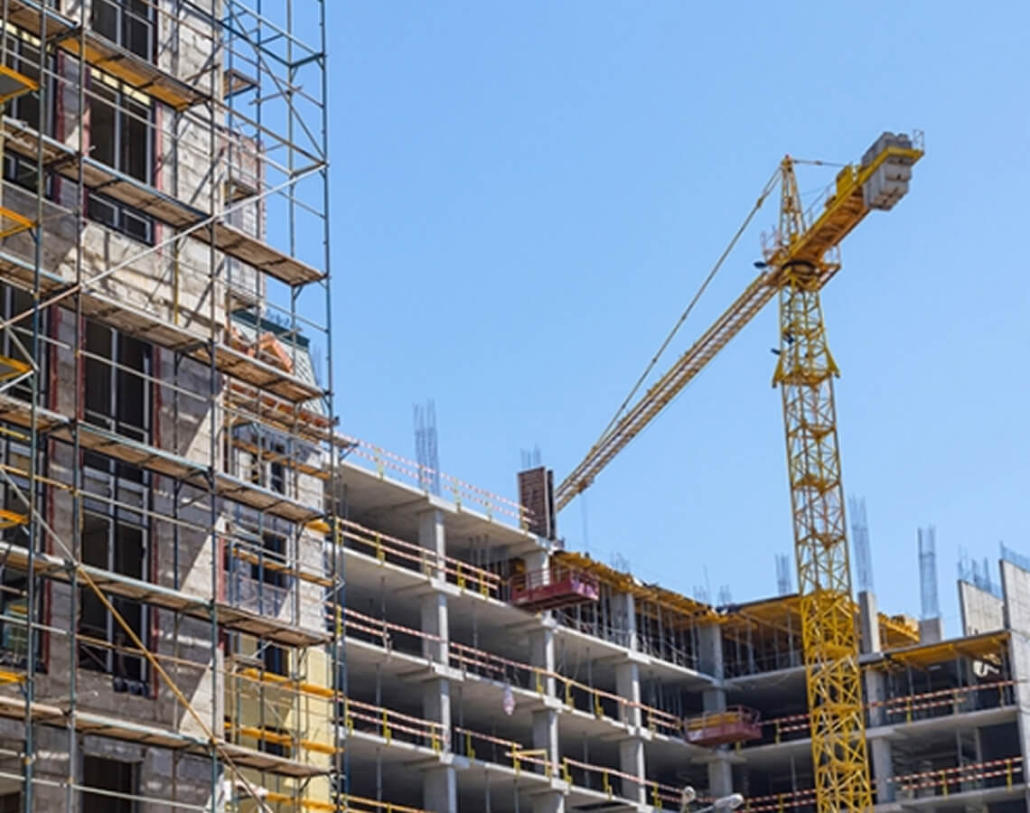 Baustelle eines Hochhauses mit unfertiger Betonstruktur, umgeben von Gerüsten, und einem großen gelben Baukran, der vor einem klaren blauen Himmel aufragt.