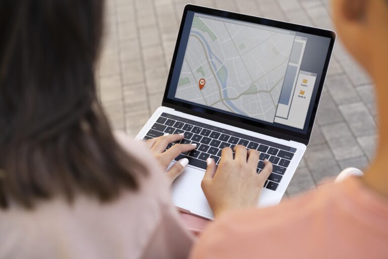 Zwei Personen betrachten einen Laptop, dessen Bildschirm eine digitale Karte mit einer roten Standortnadel und einigen Informationstafeln anzeigt. Die H&auml;nde der vorderen Person tippen auf der Tastatur.